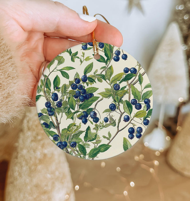 a hand holding a ceramic ornament with blue berries on it