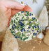a hand holding a ceramic ornament with blue berries on it