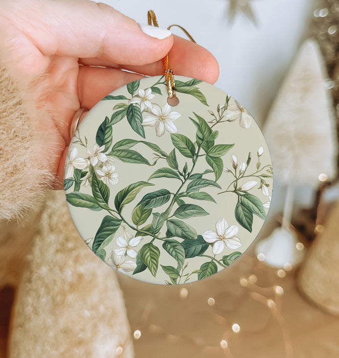 a hand holding a christmas ornament with white flowers