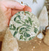 a hand holding a christmas ornament with white flowers