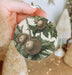 a person holding a christmas ornament with a picture of a plant on it