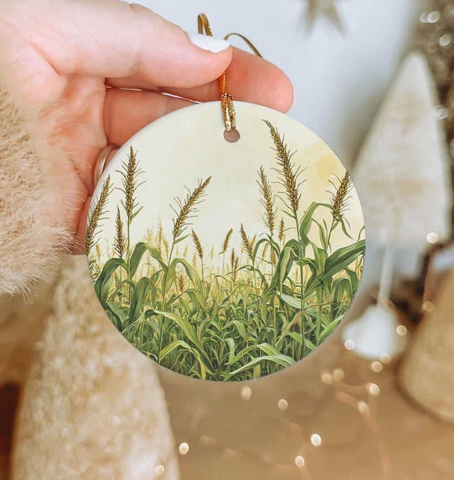 a hand holding a round ornament with a picture of a cornfield