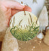 a hand holding a round ornament with a picture of a cornfield