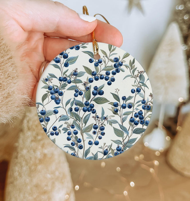 a hand holding a ceramic ornament with blue berries on it