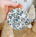 a hand holding a ceramic ornament with blue berries on it