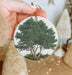a hand holding a christmas ornament with a tree on it