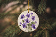 a white ornament with purple flowers hanging from a tree