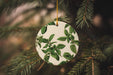a white ornament with green leaves hanging from a tree