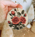 a hand holding a christmas ornament with roses on it