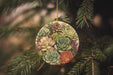 a ceramic ornament with succulents hanging from a pine tree