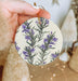 a hand holding a ceramic ornament with purple flowers