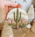 a person holding a christmas ornament with a cactus on it