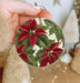 a hand holding a christmas ornament decorated with poinsettia leaves