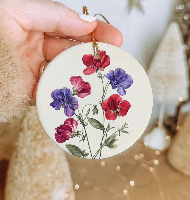 a hand holding a christmas ornament with flowers painted on it