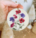 a hand holding a christmas ornament with flowers painted on it