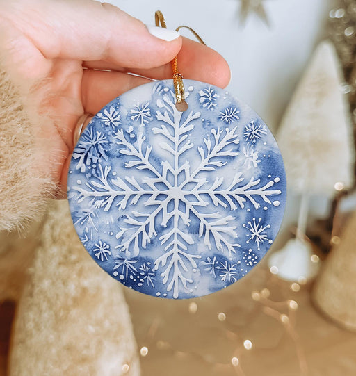 a hand holding a snowflake ornament in front of a christmas tree