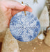 a hand holding a snowflake ornament in front of a christmas tree