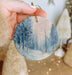 a person holding a small ornament with a snowy scene on it
