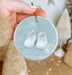 a hand holding a christmas ornament with a pair of shoes on it