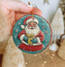 a hand holding a christmas ornament with a santa clause on it