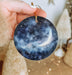 a hand holding a blue ornament with a white moon and stars on it