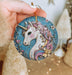 a hand holding a blue ornament with a unicorn on it