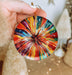 a hand holding a colorful glass ornament in front of a christmas tree