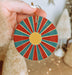 a hand holding a red, blue, and yellow ornament