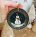 a person holding a christmas ornament with a snowman on it