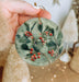a hand holding a ceramic ornament with berries on it