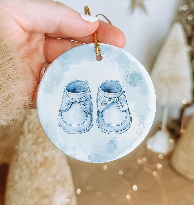 a hand holding a blue ornament with a pair of shoes on it
