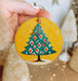 a hand holding a christmas ornament with a christmas tree on it