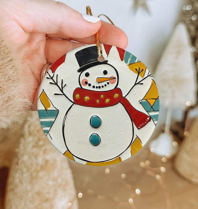 a hand holding a christmas ornament with a snowman on it