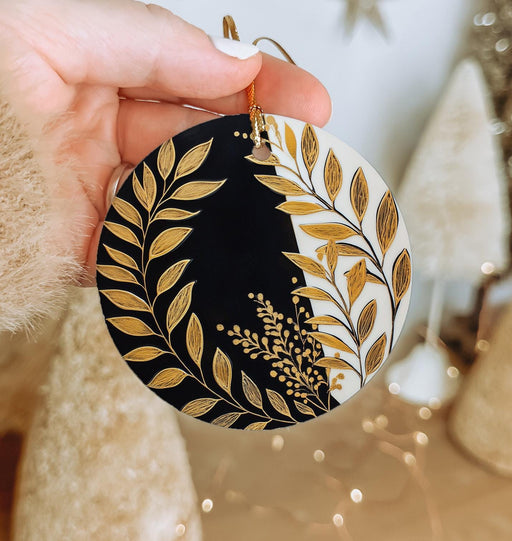 a hand holding a black and gold christmas ornament