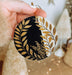a hand holding a black and gold christmas ornament