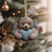 a teddy bear holding a heart ornament hanging from a christmas tree