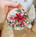 a hand holding a christmas ornament with poinsettis on it