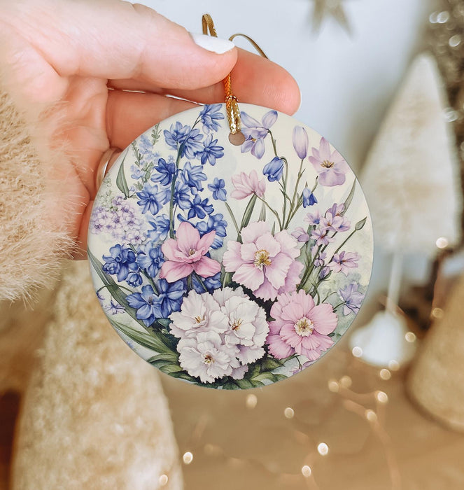 a hand holding a floral ornament in front of a christmas tree
