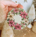 a hand holding a christmas ornament with poinsettis on it
