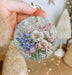 a hand holding a glass ornament with flowers on it
