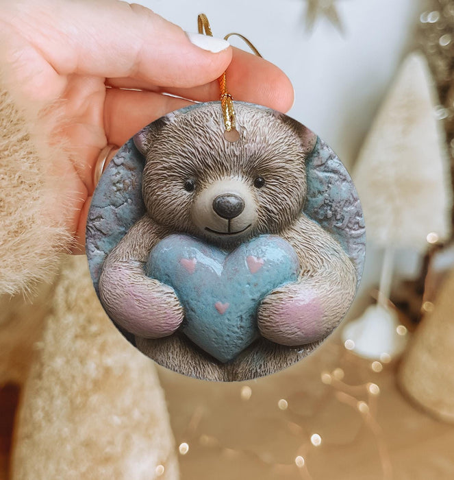 a hand holding a ceramic ornament with a teddy bear holding a heart