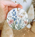 a hand holding a christmas ornament with flowers painted on it
