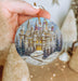 a hand holding a christmas ornament with a castle on it