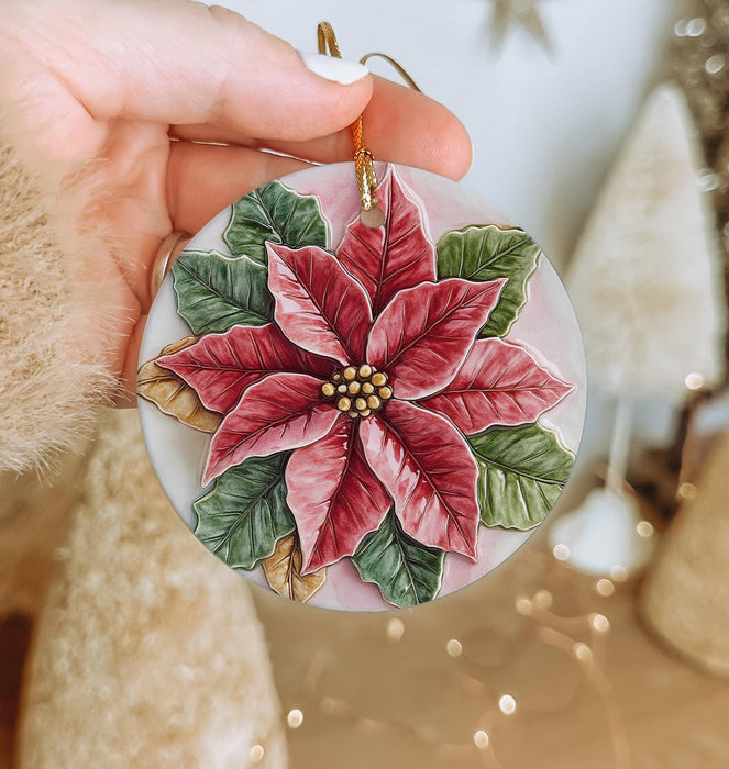 a hand holding a christmas ornament with a poinsetti on it
