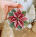 a hand holding a christmas ornament with a poinsetti on it
