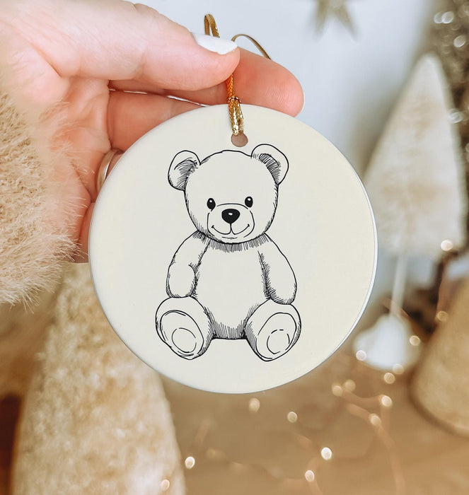 a hand holding a christmas ornament with a drawing of a teddy bear