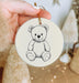 a hand holding a christmas ornament with a drawing of a teddy bear