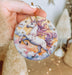 a hand holding a round ornament with a unicorn on it