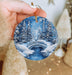 a person holding a christmas ornament with a snowy scene on it