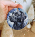 a hand holding a christmas ornament with a black dog on it